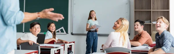 Alegre multiétnicos compañeros de clase mirando borrosa maestra, pancarta - foto de stock