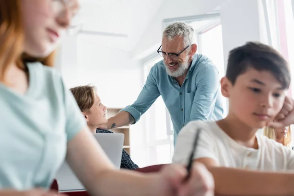 Enseignant positif regardant un écolier près d'élèves multiethniques — Photo de stock