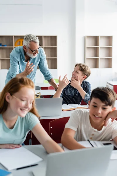 Веселий вчитель і школяр розмовляє поблизу багатоетнічних однокласників — стокове фото