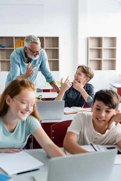 Alegre maestro y colegial hablando cerca de compañeros de clase multiétnicos - foto de stock