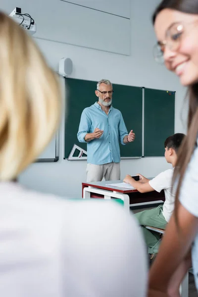 Reife Lehrer reden in der Nähe von Schülern im Klassenzimmer — Stockfoto