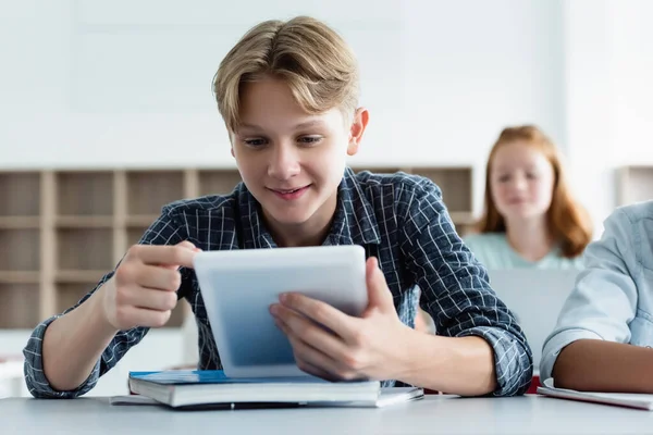 Écolier souriant utilisant une tablette numérique près d'un ordinateur portable — Photo de stock