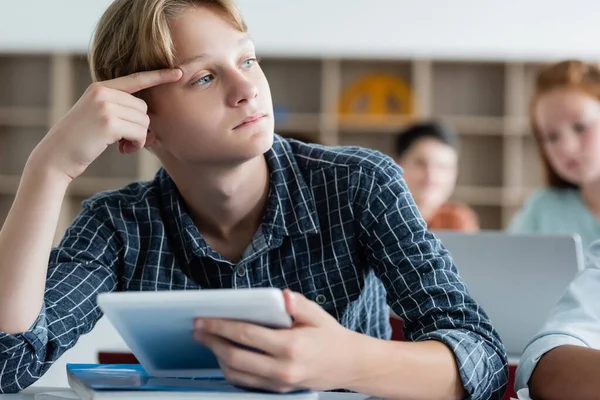Pensive écolier tenant tablette numérique dans la classe — Photo de stock