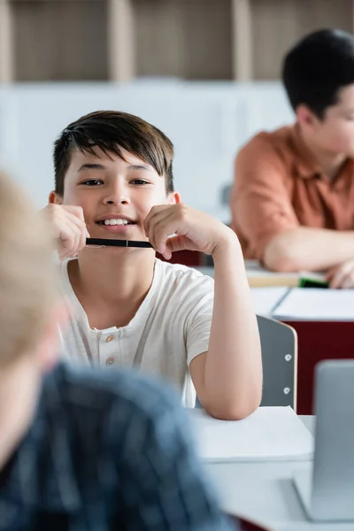 Smiling asian schoolboy holding pen in classroom — Stock Photo