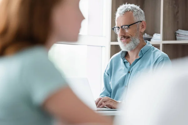 Professor feliz usando laptop perto de criança turva em sala de aula — Stock Photo