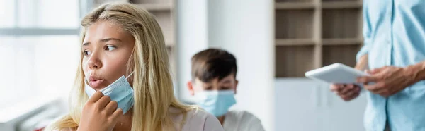 Niño de la escuela sosteniendo máscara médica y respirando en el aula, pancarta - foto de stock