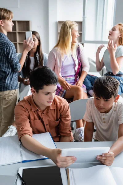Écoliers multiethniques regardant tablette numérique près des camarades de classe — Photo de stock
