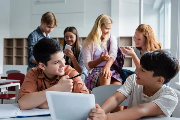 Cheerful asian child holding digital tablet near friend and classmates — Stock Photo