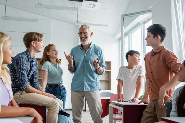 Mature professeur pointant du doigt près de joyeux enfants multiethniques — Photo de stock