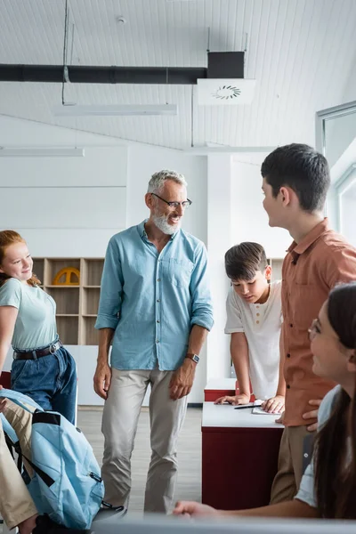 Mature teacher smiling near multicultural teenagers in classroom — Stock Photo
