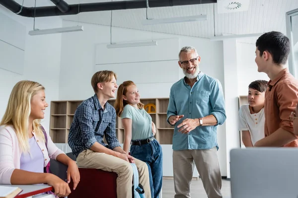 Profesor sonriente haciendo gestos mientras habla con alumnos multiétnicos en el aula — Stock Photo