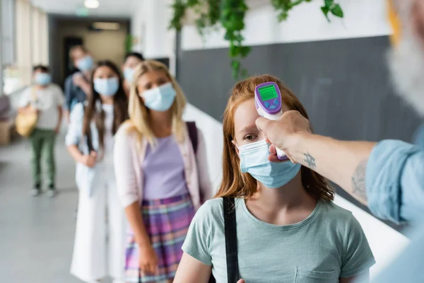 Foyer sélectif du pyromètre en main de l'enseignant vérifiant la température des élèves faisant la queue dans les masques médicaux — Photo de stock