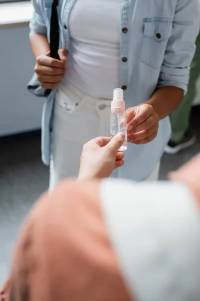 Cropped view of blurred teenager giving hand sanitizer to schoolgirl — Stock Photo