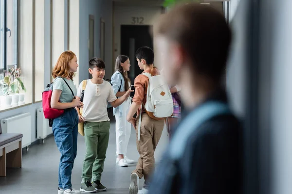 Ragazzo sfocato in piedi da solo vicino ai compagni di classe parlando nel corridoio della scuola — Foto stock