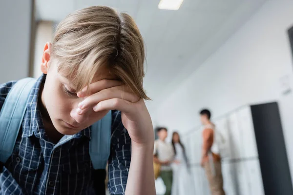 Frustrado adolescente con la cabeza inclinada cerca de compañeros de clase en fondo borroso - foto de stock