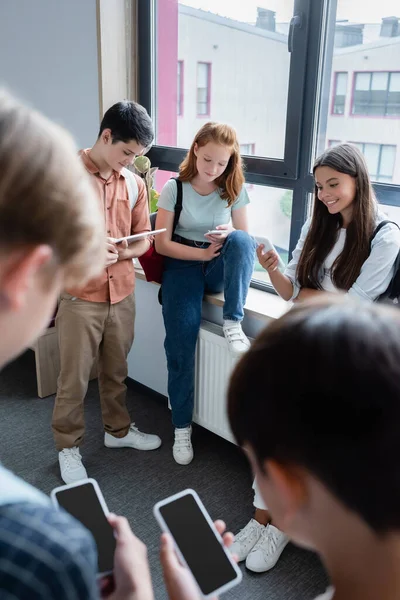 Alumnos adolescentes que utilizan dispositivos en el pasillo escolar en primer plano borroso - foto de stock