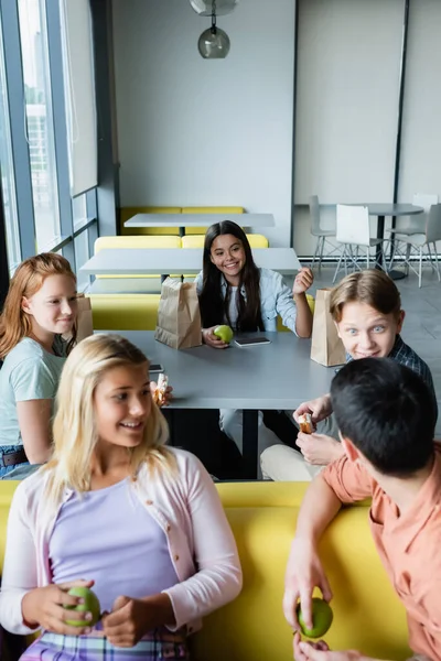 Adolescentes alegres hablando durante la pausa del almuerzo en el comedor de la escuela - foto de stock
