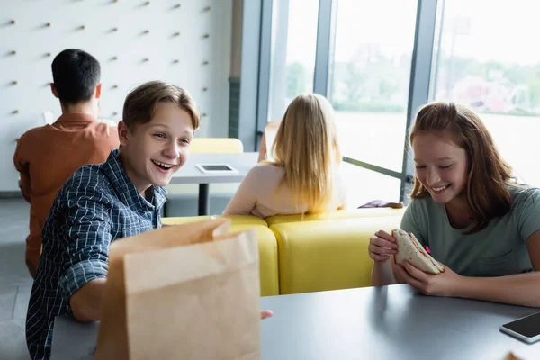 Pupilos adolescentes sonriendo durante la pausa para el almuerzo en el comedor escolar - foto de stock