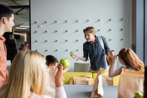 Cheerful boy gesturing while talking to classmates in school eatery — Stock Photo