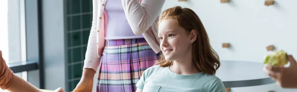 Rossa ragazza sorridente vicino ai compagni di classe nella sala da pranzo della scuola, banner — Foto stock