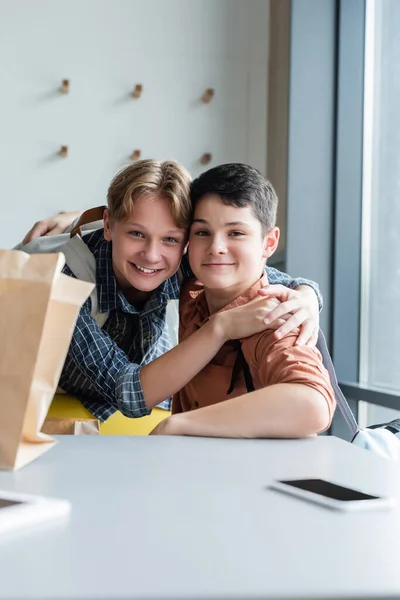 Glückliche Teenager gucken in die Kamera, während sie sich im Schulspeiseraum umarmen — Stockfoto