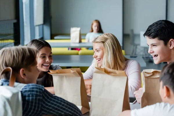 Adolescentes felices hablando en el comedor de la escuela, mientras que la chica deprimida sentado solo sobre fondo borroso - foto de stock
