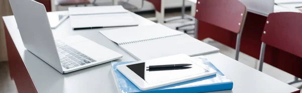 Tableta digital y portátil cerca de portátiles en el escritorio en la escuela moderna, bandera - foto de stock