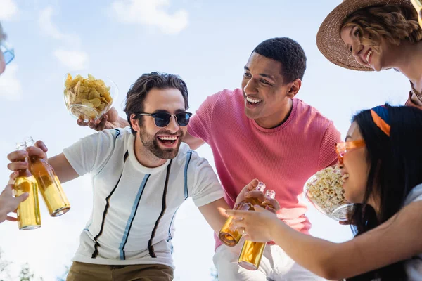 Tiefansicht eines fröhlichen Mannes mit Sonnenbrille, der Bier in der Nähe multiethnischer Freunde hält — Stockfoto