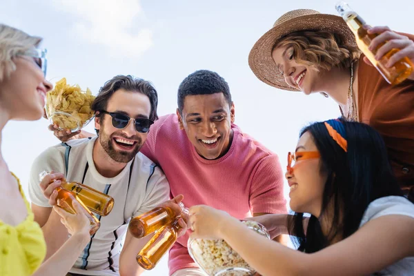 Feliz interracial homens propondo pipocas e cerveja para sorrir mulheres — Fotografia de Stock