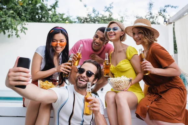 Человек в солнечных очках делает селфи с радостными мультикультурными друзьями во время летней вечеринки — стоковое фото