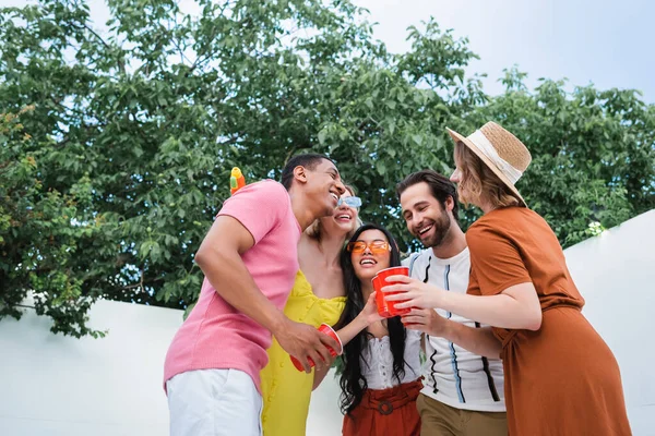 Jovens e felizes amigos multiétnicos abraçando durante a festa de verão no pátio — Fotografia de Stock