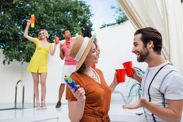 Lächelnder Mann prostet Frau mit Strohhut bei Party mit multiethnischen Freunden zu — Stockfoto