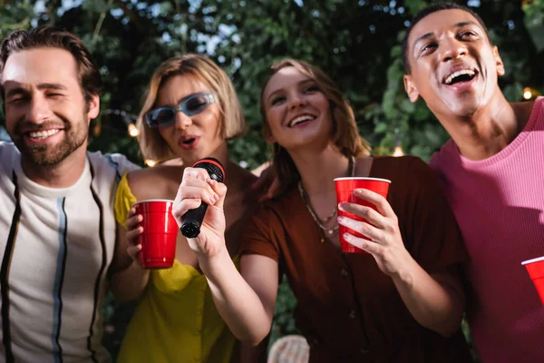 Ami multiethnique joyeux avec des tasses en plastique chantant karaoké en plein air — Photo de stock