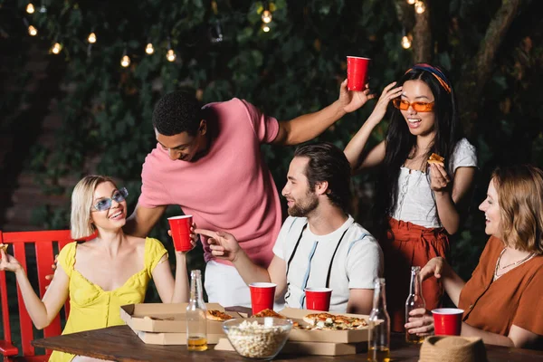 Giovane uomo che punta con il dito ad un amico con tazza di plastica vicino a persone multietniche e cibo all'aperto — Foto stock