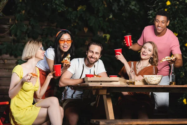 Щасливі мультикультурні друзі з пивом і їжею дивляться на камеру під час літньої вечірки — стокове фото