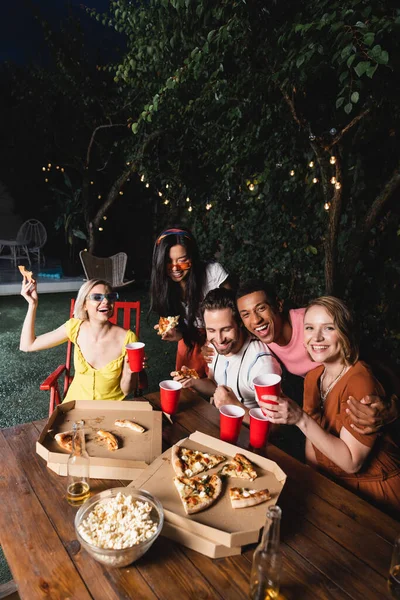 Amigos multiétnicos felizes com cerveja, pizza e pipocas se divertindo durante a festa de verão — Fotografia de Stock