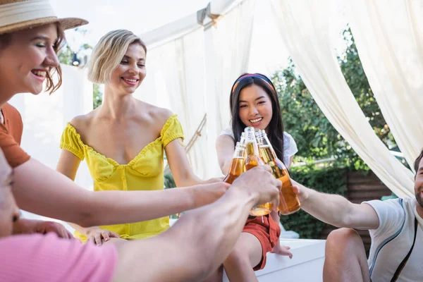 Happy multiethnic people clinking with bottles of beer in patio — Stock Photo