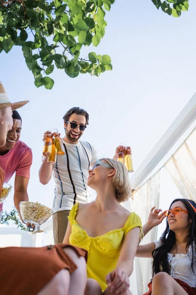 Низький кут зору людини, що тримає пиво біля багатоетнічних друзів у патіо — стокове фото