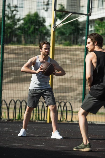 Mann hält Basketballball neben verschwommenem Freund auf Spielplatz — Stockfoto