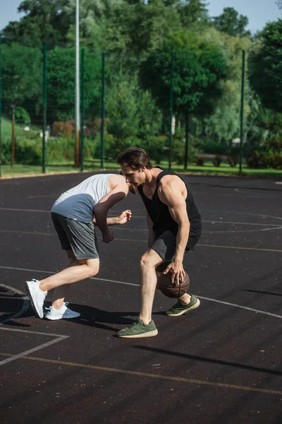 Молодой человек играет в стритбол с другом на открытой площадке — стоковое фото