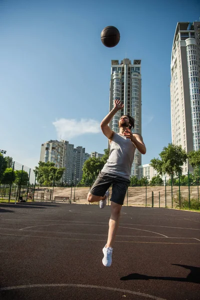 Jogador pulando e jogando bola de basquete no campo durante o dia — Fotografia de Stock