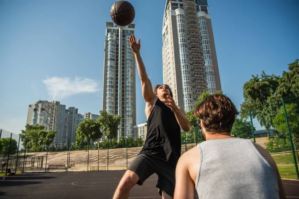 Deportista saltando cerca de pelota de baloncesto y amigo al aire libre - foto de stock