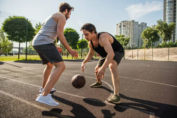 Вид сбоку на мужчин в спортивной одежде, играющих в баскетбол на открытом воздухе — стоковое фото