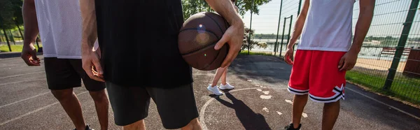 Vista ritagliata dello sportivo con pallone da basket in piedi vicino agli amici interrazziali, banner — Foto stock