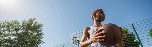 Vue à angle bas du joueur afro-américain tenant le ballon de basket à l'extérieur, bannière — Photo de stock