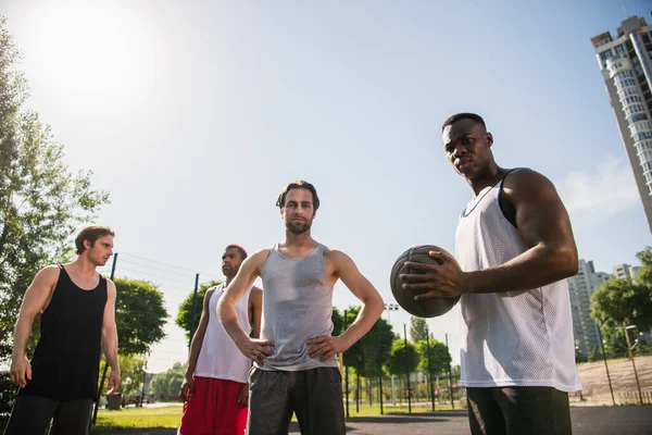 Vue à angle bas des joueurs de basket interracial regardant la caméra à l'extérieur — Photo de stock