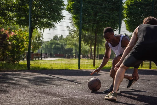 Deportista afroamericano jugando streetball cerca de amigo en patio de recreo — Stock Photo