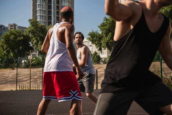 Deportista afroamericano de pie cerca de un amigo con pelota durante la competición de baloncesto - foto de stock