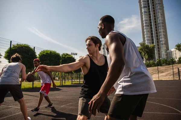 Hommes interraciaux regardant des amis pendant le jeu de basket en plein air — Photo de stock