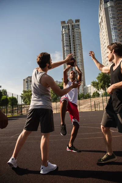 Joueur afro-américain tenant le ballon de basket tout en jouant avec des amis sur l'aire de jeux — Photo de stock